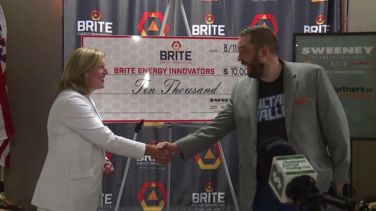 BRITE president and CEO shakes hands with Alexa Sweeney in front of a large check to BRITE for $10,000.