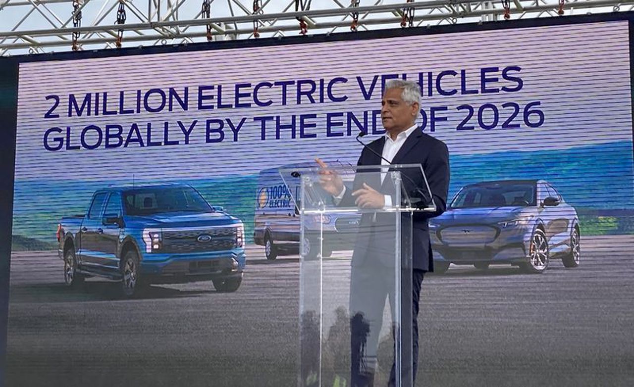 Man presenting at an industry event in front of a sign that reads, "2 million electric vehicles globally by the end of 2026"